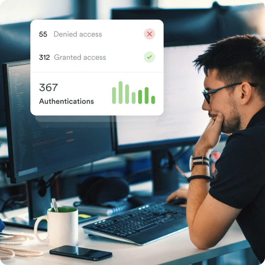 Man at a desk with dual monitors views authentication stats: 55 denied, 312 granted, 367 total