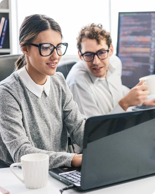 Woman on her laptop with a coffee mug on one side and a man on the other side looking at the content on her screen