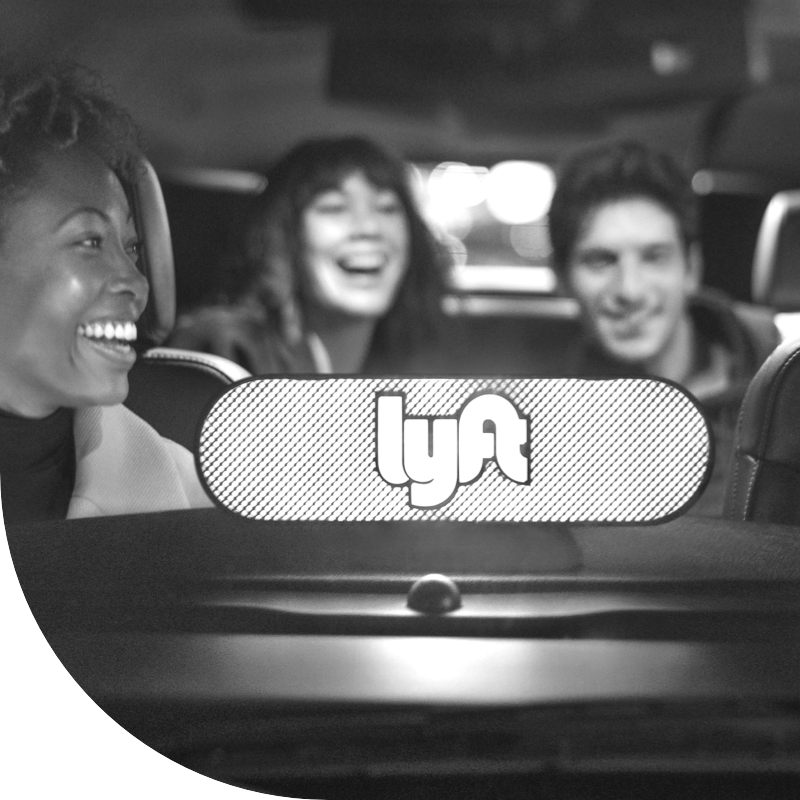 Three people in a vehicle with a Lyft sign in the window.