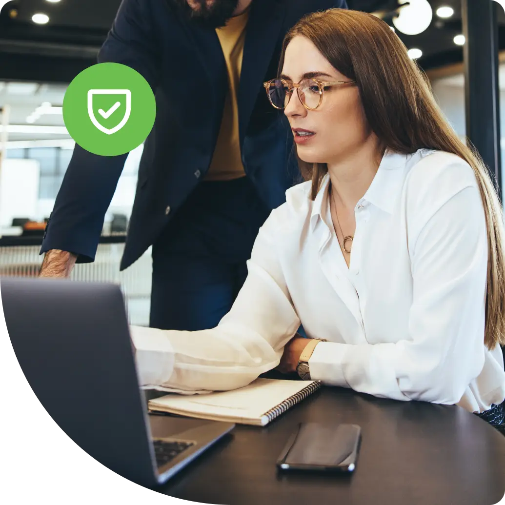 Two IT professionals collaborating at a laptop while a colleague works in the background