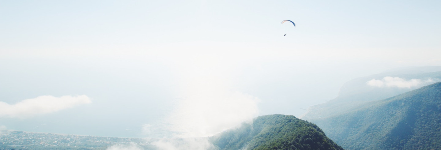 A beautiful, cloudy mountain view with a skydiver hovering above.