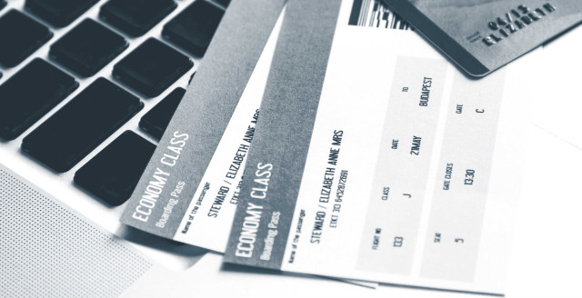 Two economy-class airline tickets lie beneath a credit card and over a keyboard.