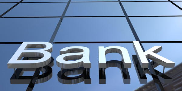 On the side of a shiny-windowed skyscraper, the word Bank appears in large three-dimensional letters.