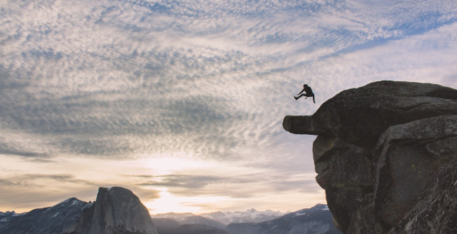 A person leaps in the air atop a high boulder, representing overcoming fear, uncertainty and doubt.
