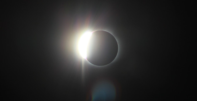A solar eclipse is nearly complete, with one side still glaringly bright.