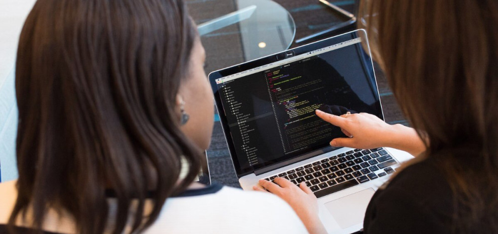 Two women discussing code on a laptop screen.